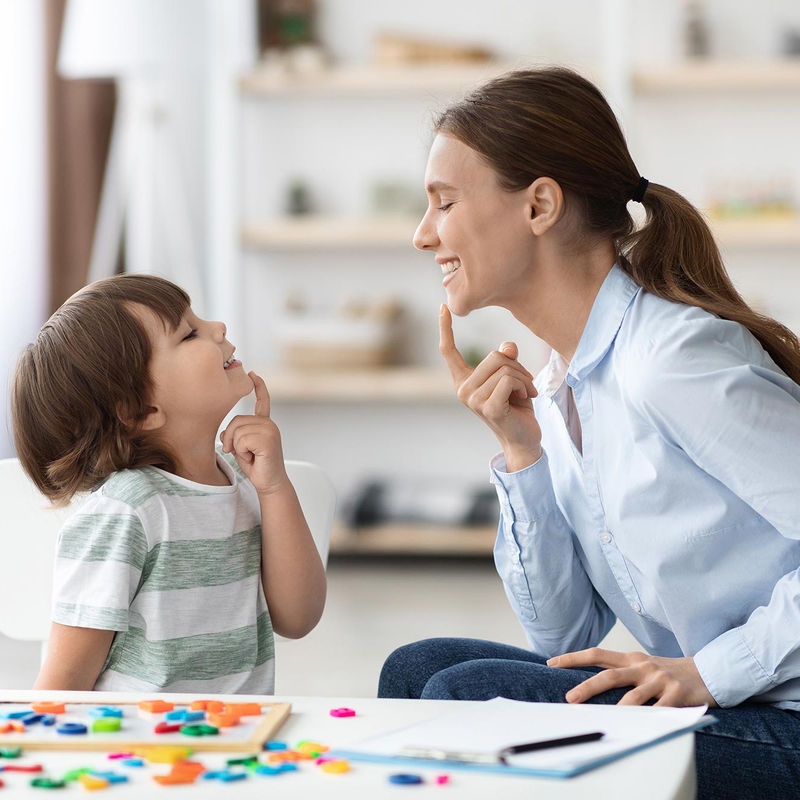 Un niño y su terapeuta practicando habilidades de comunicación en una mesa